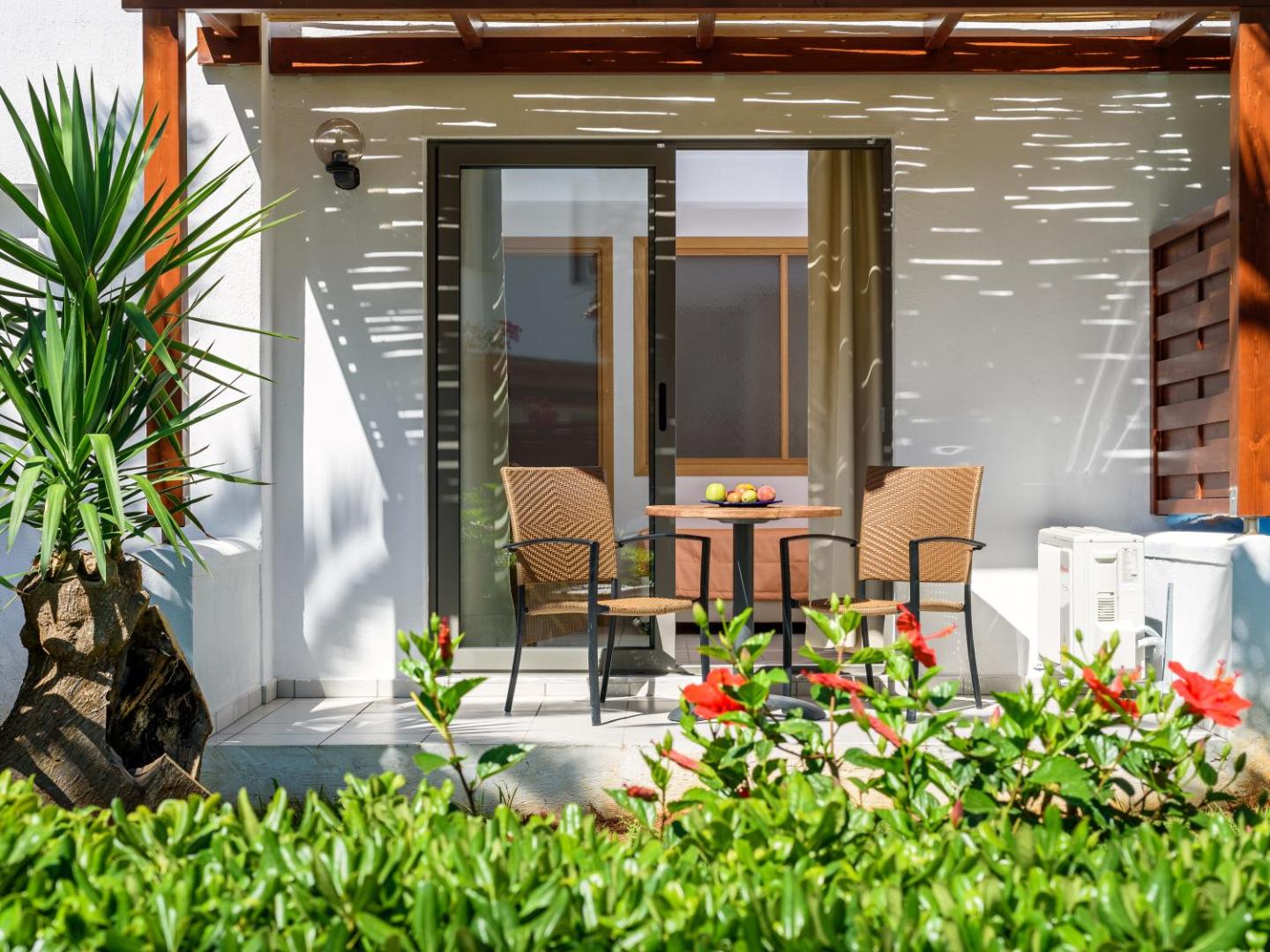 Annabelle Beach Resort numura ieeja no dārza puses ar stikla bīdāmajām durvīm, āra mēbelēm un ziedošiem krūmiem priekšplānā.