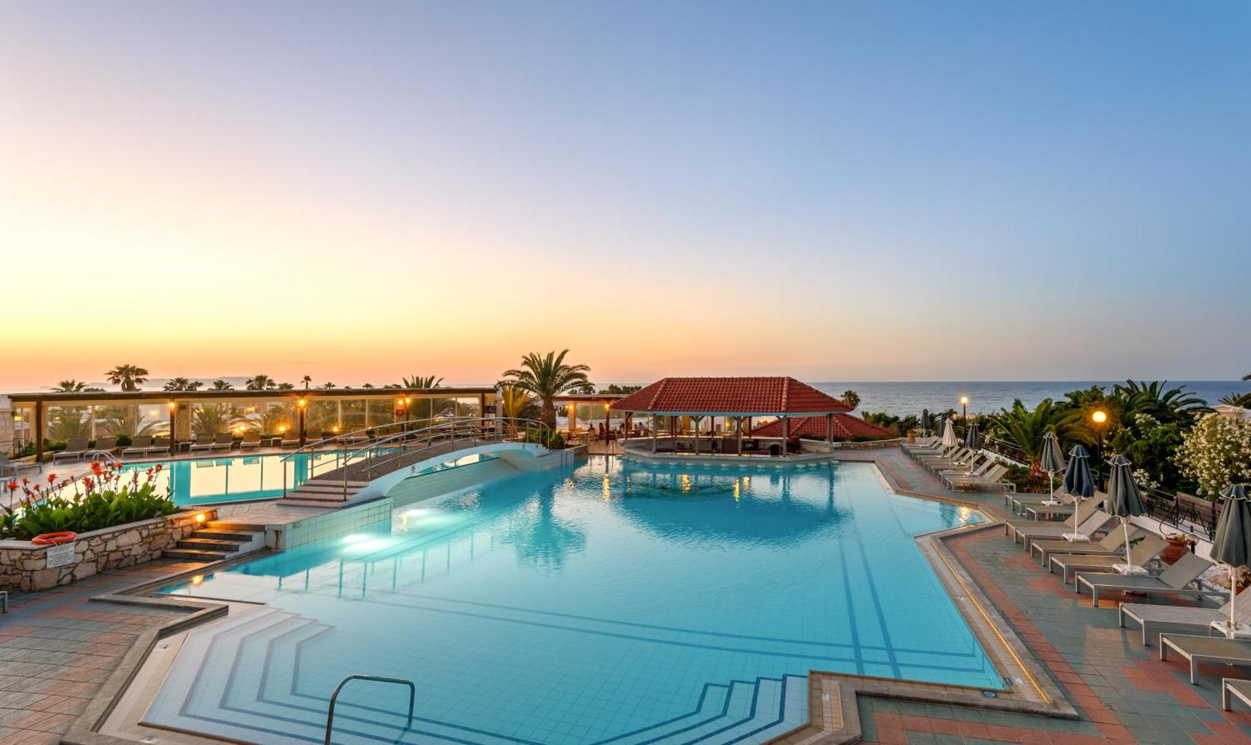 Annabelle Beach Resort baseina komplekss ar tiltiņu un bāru piekrastē — panorāmas skats uz jūru un kūrorta teritoriju saulrietā