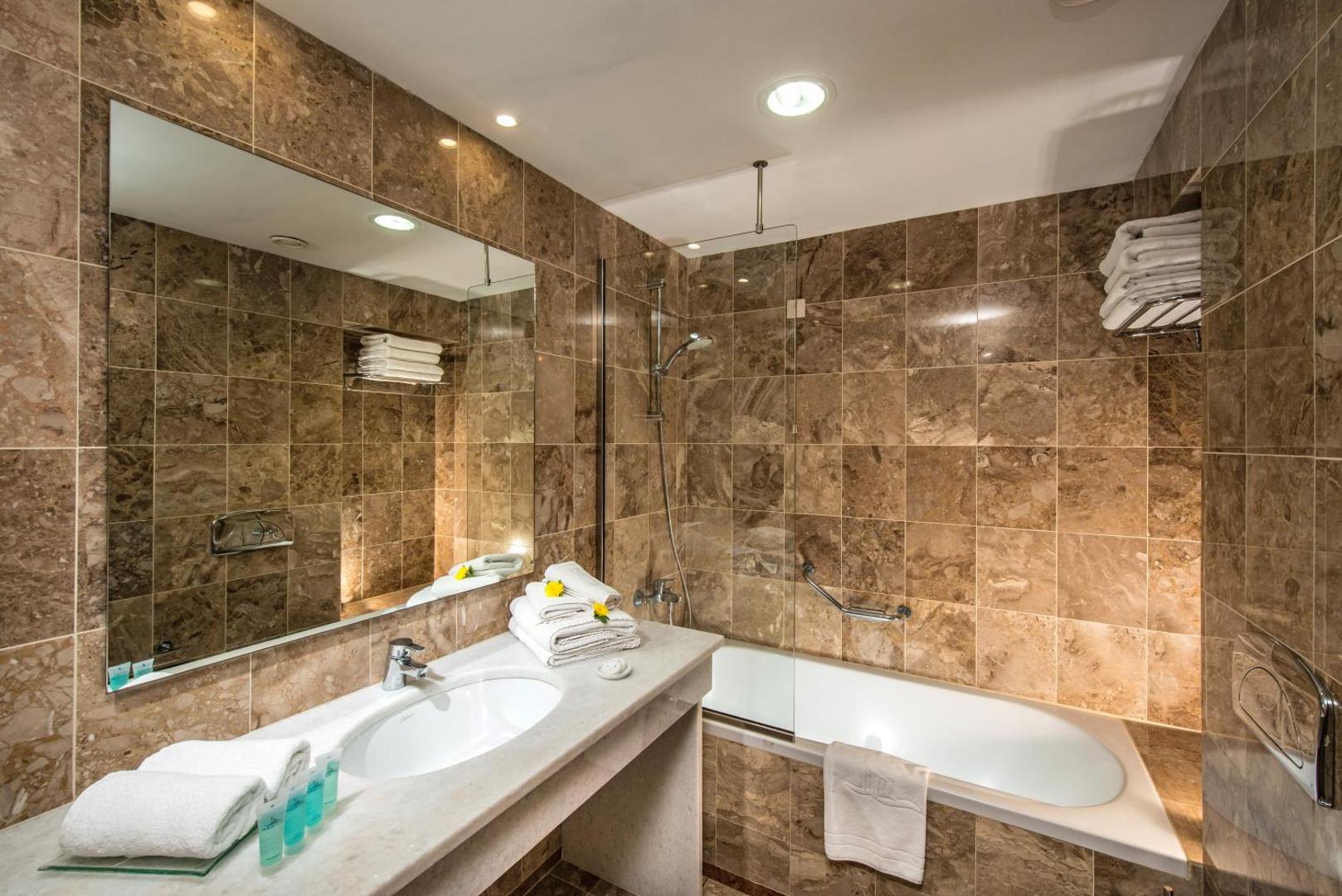 Annabelle Beach Resort numura vannas istaba ar marmora apdari, vannu, lielu spoguli un gaišu apgaismojumu Krētā.