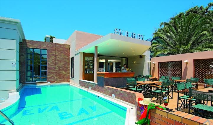 Eva Bay Hotel bārs pie baseina ar āra terasi un galdiņiem — gaiša arhitektūra un tirkīzzils ūdens Krētas kūrortā