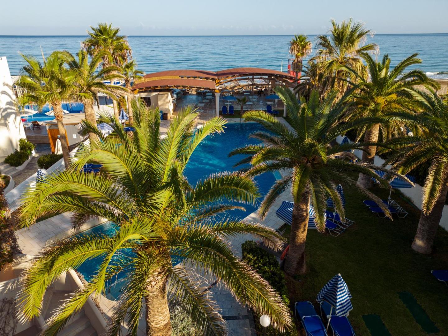 Eva Bay Hotel āra baseins un dārzs ar palmām Adelianos Kamposā, Krētā — skats uz jūras piekrasti un sauļošanās zonu
