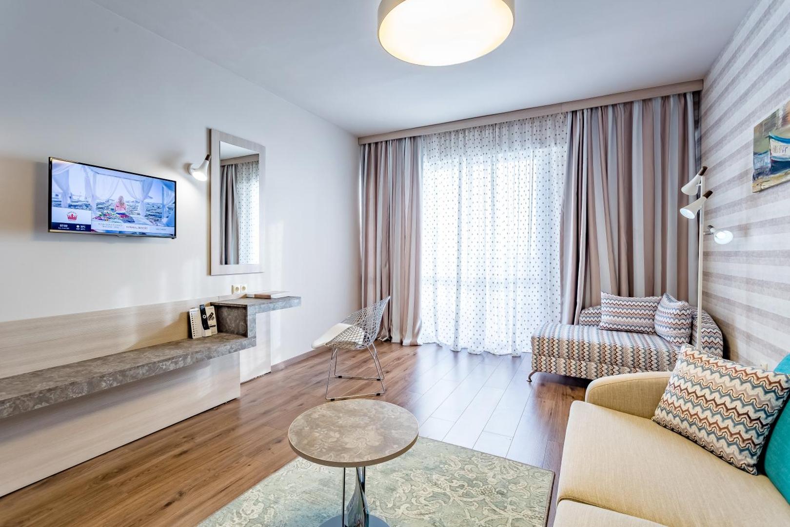 Imperial Resort numura interjers ar koka grīdu, dīvānu, kafijas galdiņu un lieliem logiem, kas nodrošina dabisku apgaismojumu
