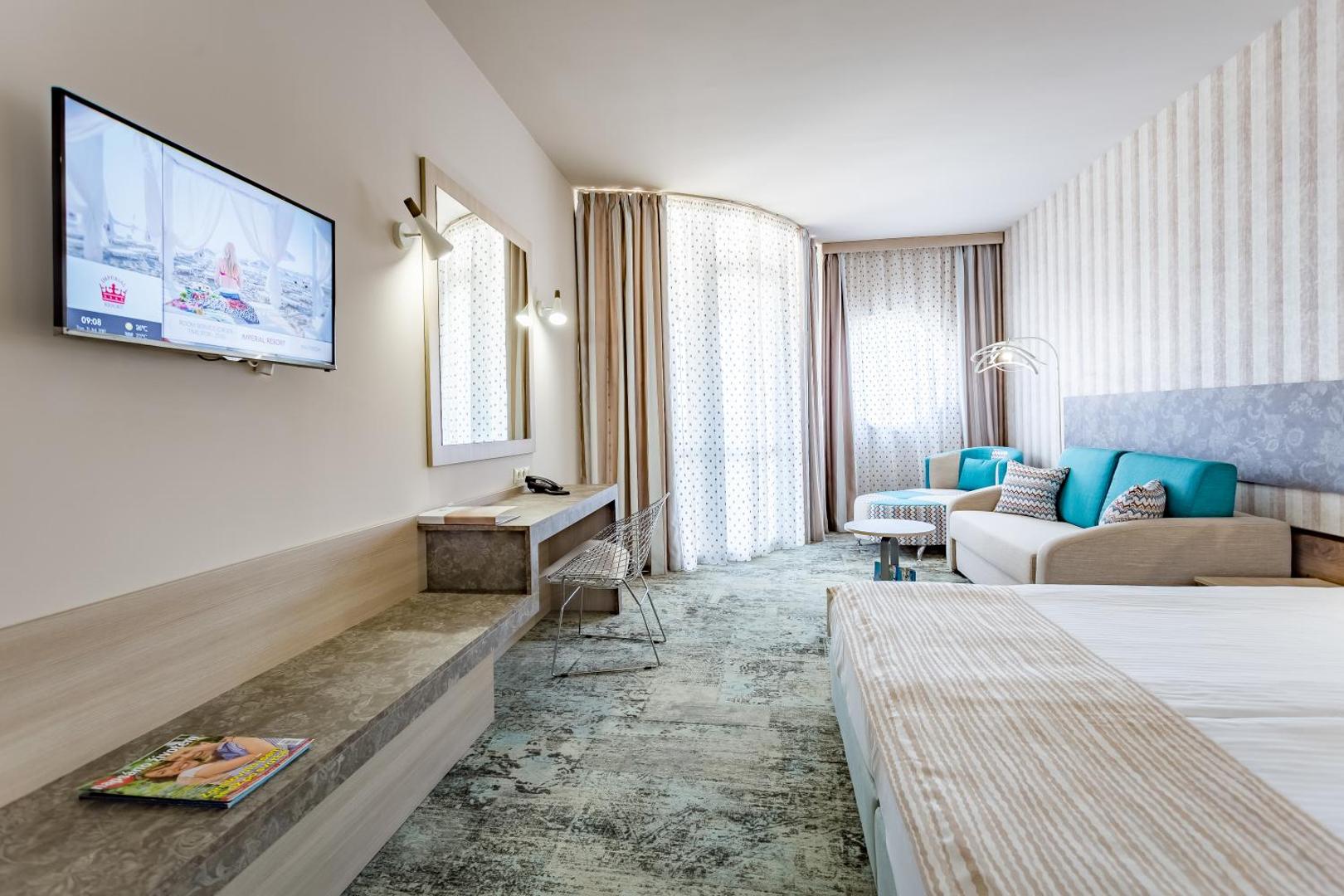 Imperial Resort gaišs viesnīcas numurs ar divguļamo gultu, atpūtas zonu, dīvānu un sienas televizoru Saulainajā Krastā, Bulgārijā