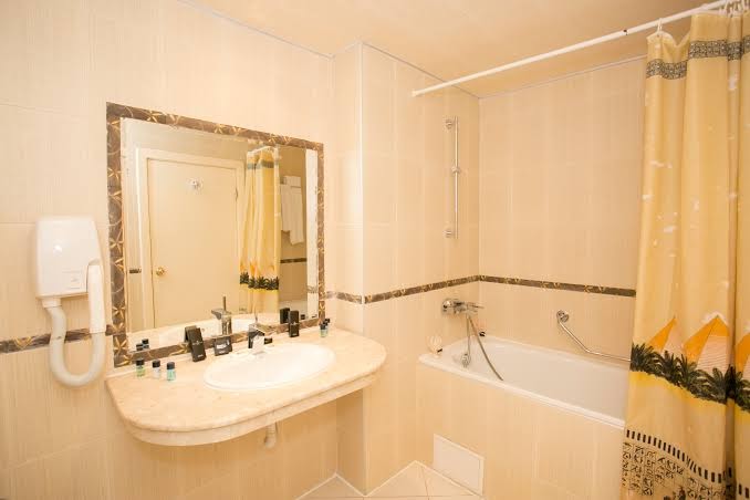 Imperial Resort numura vannas istaba ar vannu, gaišām flīzēm, plašu izlietnes virsmu un dekoratīvu aizkaru.