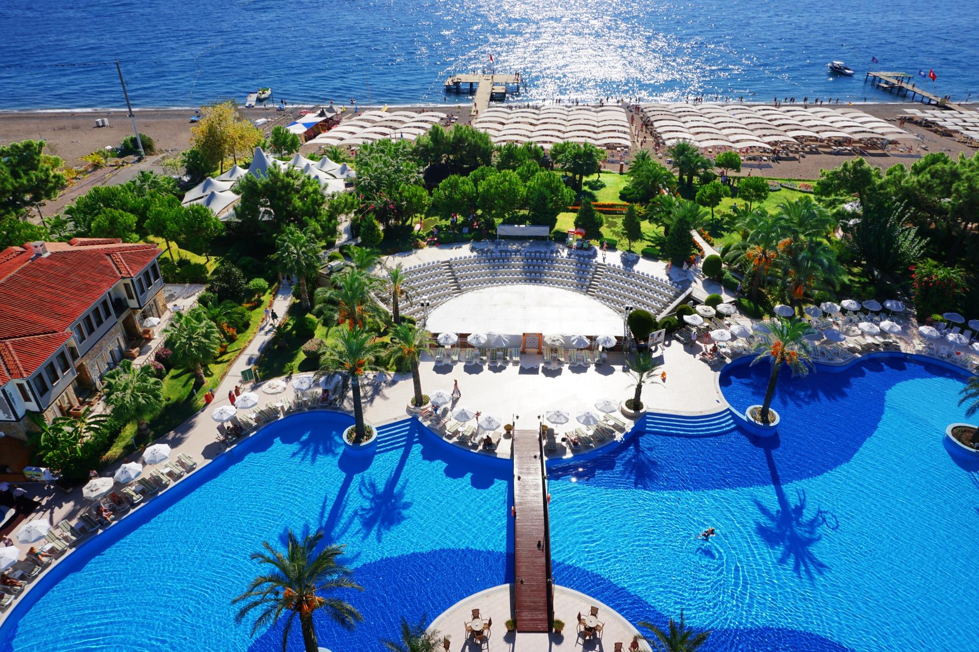 Rai Premium Tekirova panorāmas skats uz plašo baseinu, amfiteātri un privāto pludmali ar piestātni Tekirovas ciemā.