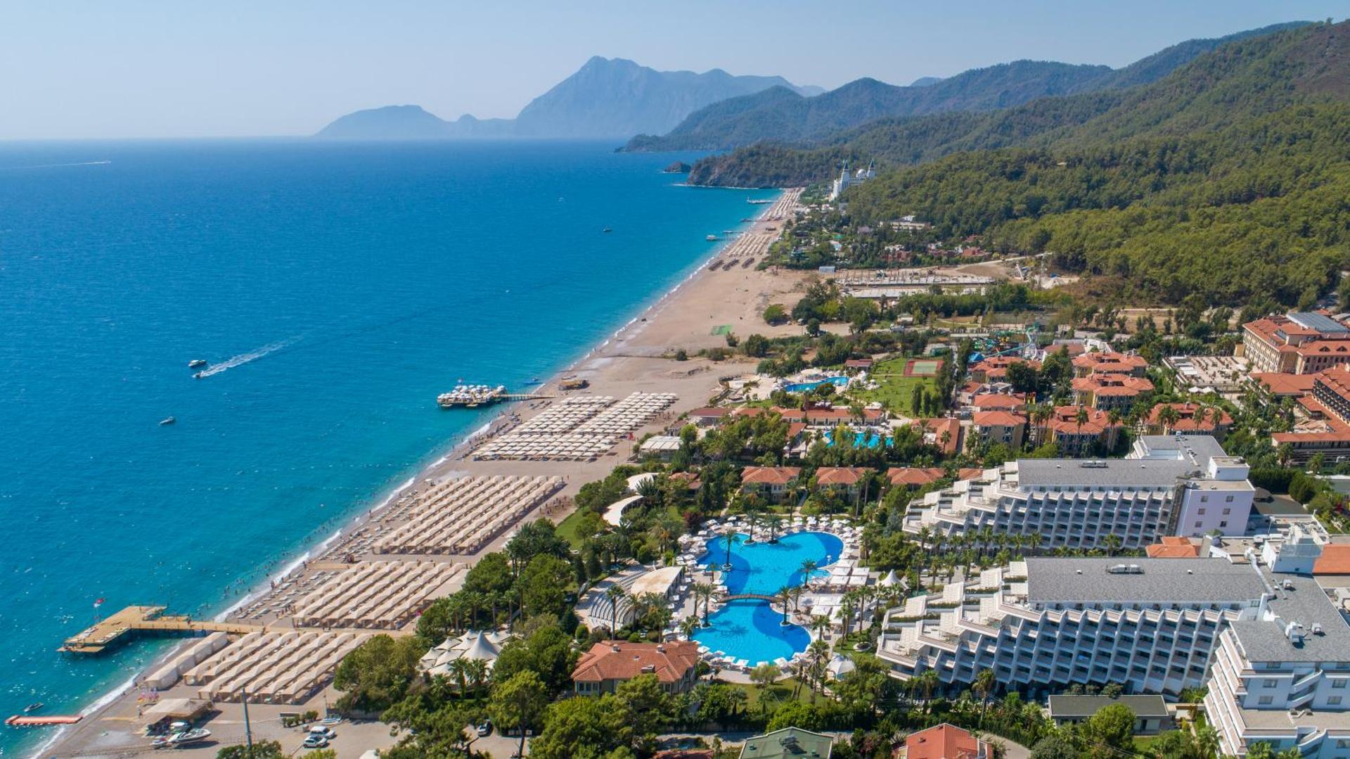 Rai Premium Tekirova panorāmas skats no putna lidojuma uz plašo pludmali, zilo Vidusjūru un viesnīcas teritoriju ar baseiniem Kemeras reģionā