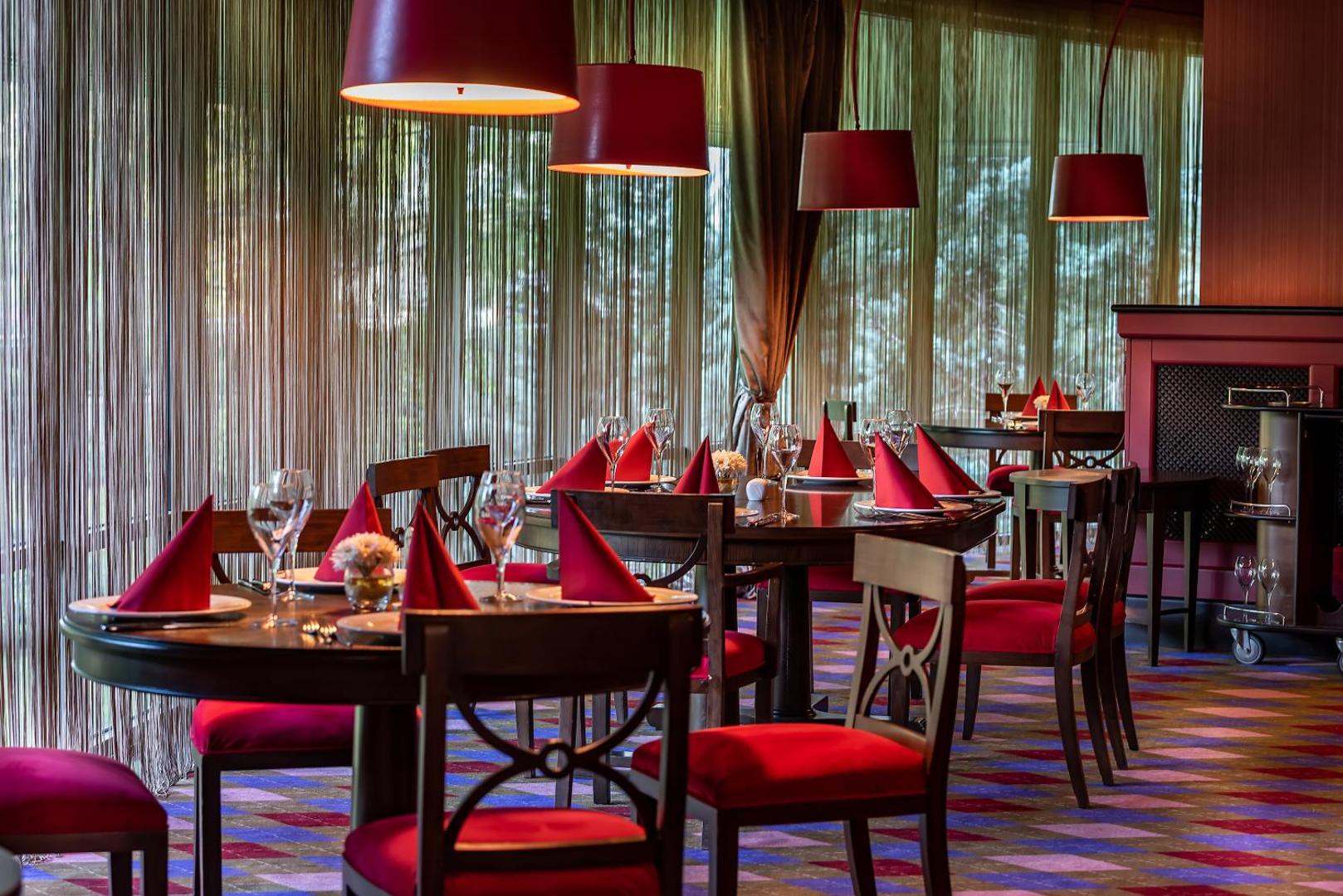 Cornelia Diamond Golf Resort & Spa eleganta restorāna iekštelpas ar sarkaniem akcentiem, apaļiem galdiem un dizaina gaismekļiem