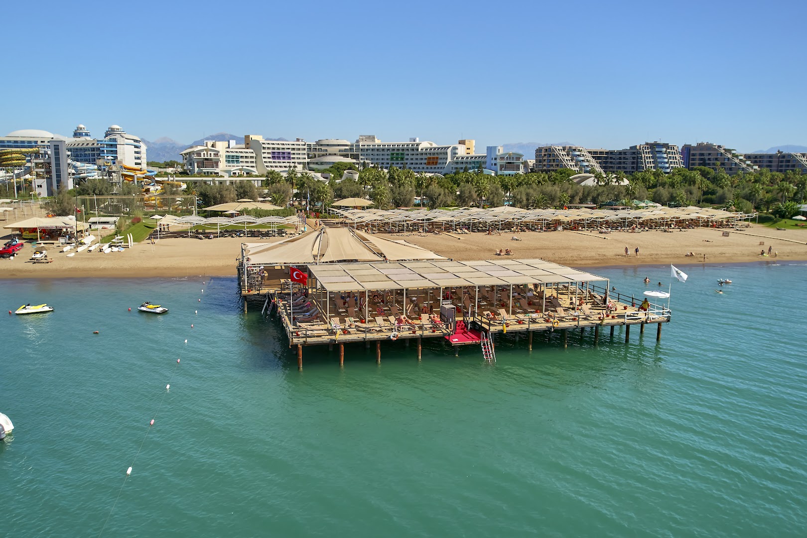 Cornelia Diamond Golf Resort & Spa panorāmas skats uz privāto pludmali, piestātni ar atpūtas zonu un viesnīcas kompleksu Belekā