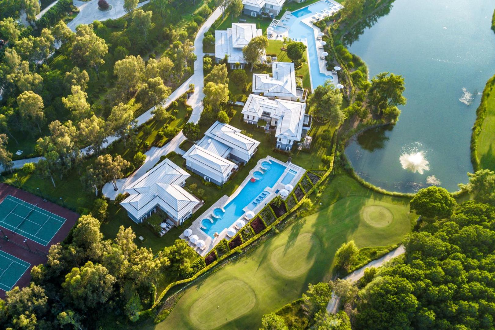 Cornelia Diamond Golf Resort & Spa aerofoto ar golfa laukumiem, ezeru, tenisa kortiem un villu kompleksu priežu meža ielokā