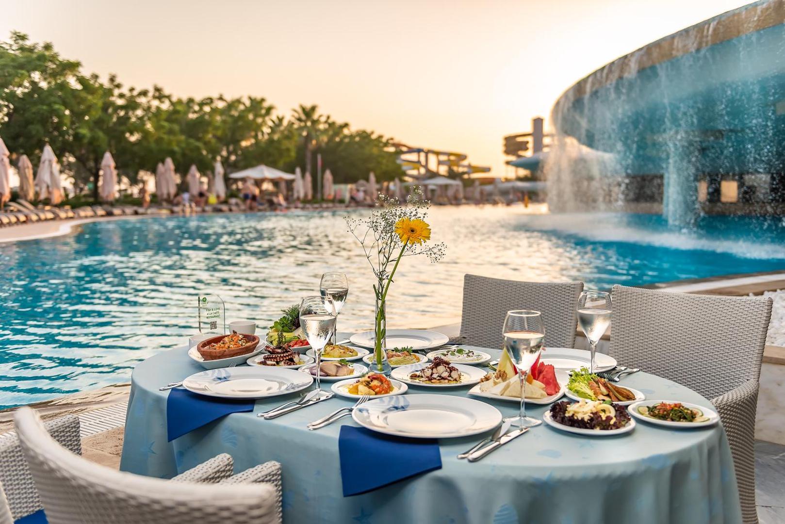 Cornelia Diamond Golf Resort & Spa restorāna galds pie baseina ar jūras velšu uzkodām un dekoratīvu ūdenskritumu fonā Belekā
