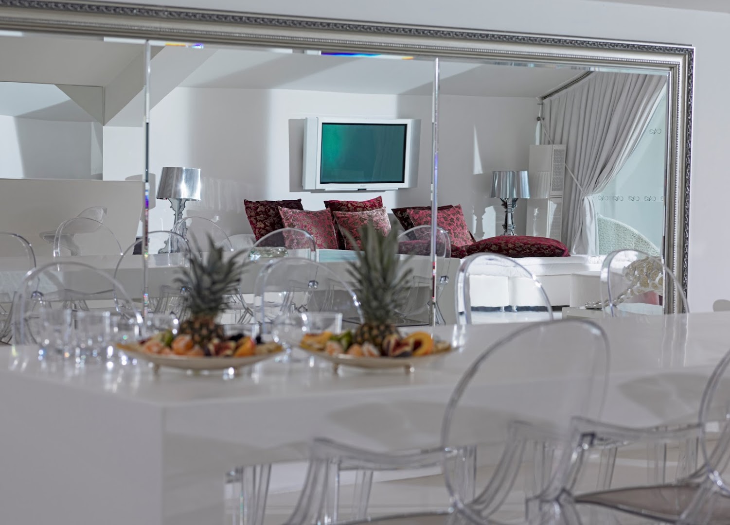 Dobedan Exclusive Hotel & Spa modernā ēdamistaba ar caurspīdīgiem krēsliem, lielu spoguli un augļu platēm uz galda