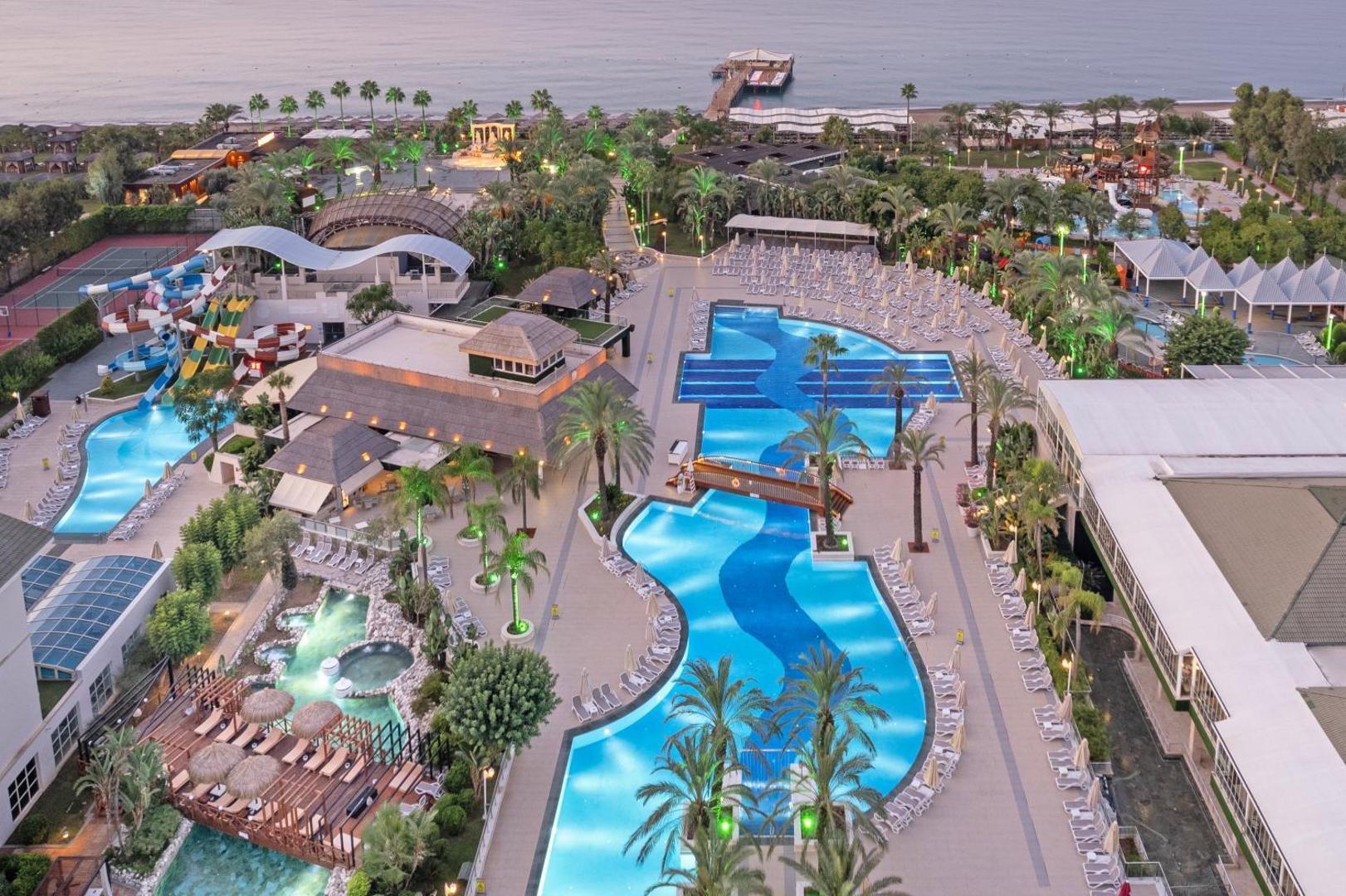 Dobedan Exclusive Hotel & Spa teritorijas skats no augšas vakarā — baseini, akvaparks un pludmales zona Belekā, Turcijā