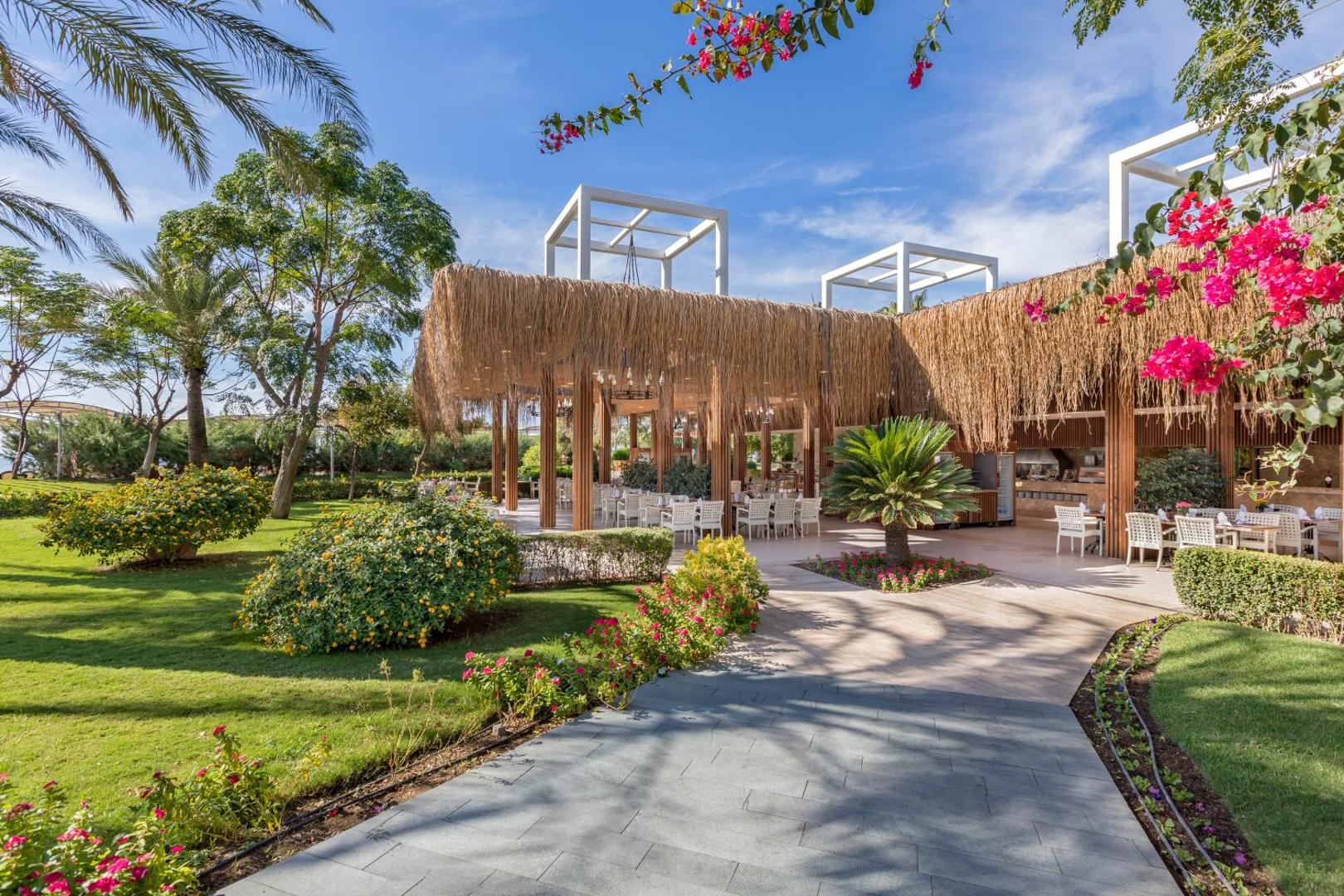 Dobedan Exclusive Hotel & Spa dārza restorāns ar salmu jumta dekorācijām, ziedošiem krūmiem un koptu zālienu