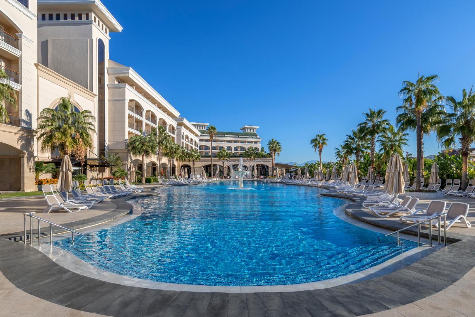 Dobedan Exclusive Hotel & Spa galvenais āra baseins ar strūklaku un viesnīcas fasādi Belekas reģionā saulainā dienā