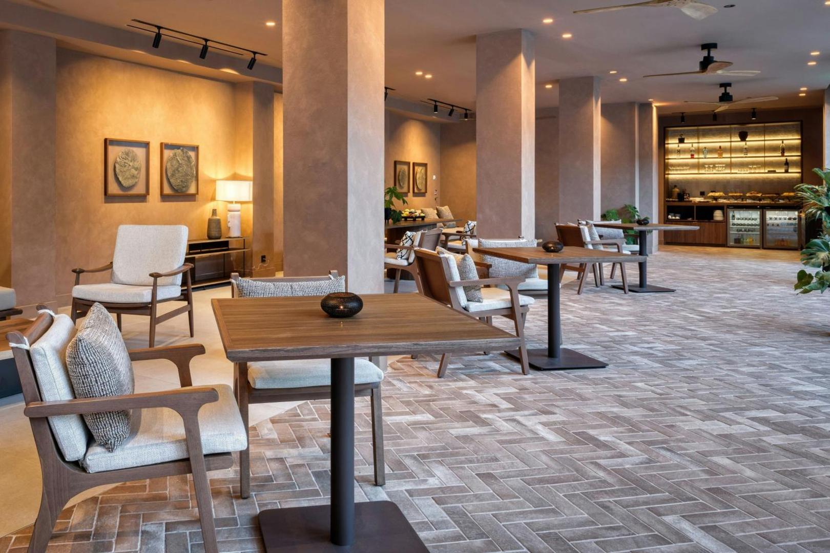 Domes of Corfu Autograph Collection modernā lobby atpūtas zona ar stilīgām mēbelēm, koka galdiem un siltu apgaismojumu