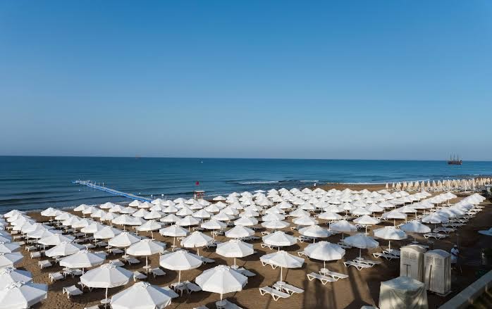 Plašs skats uz Barut Hemera pludmali ar sakārtotām saulessargu rindām un zilo jūras horizontu Turcijā.