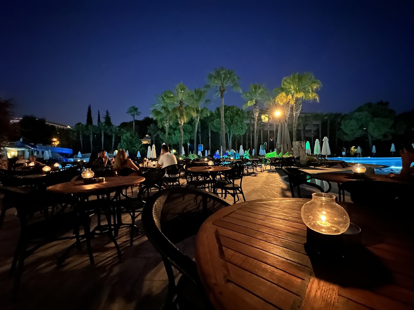 Barut Hemera vakara atmosfēra pie baseina ar izgaismotiem galdiņiem, svecēm un palmām nakts debesu fonā