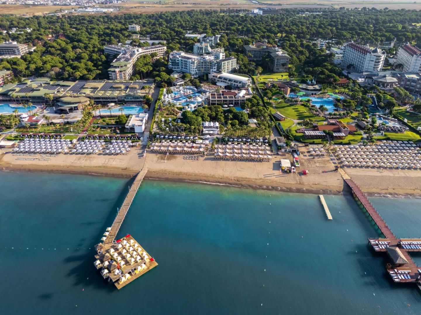 Panorāmas skats uz Limak Atlantis De Luxe teritoriju, diviem koka tiltiem jūrā un plašo smilšu pludmali Belekā.