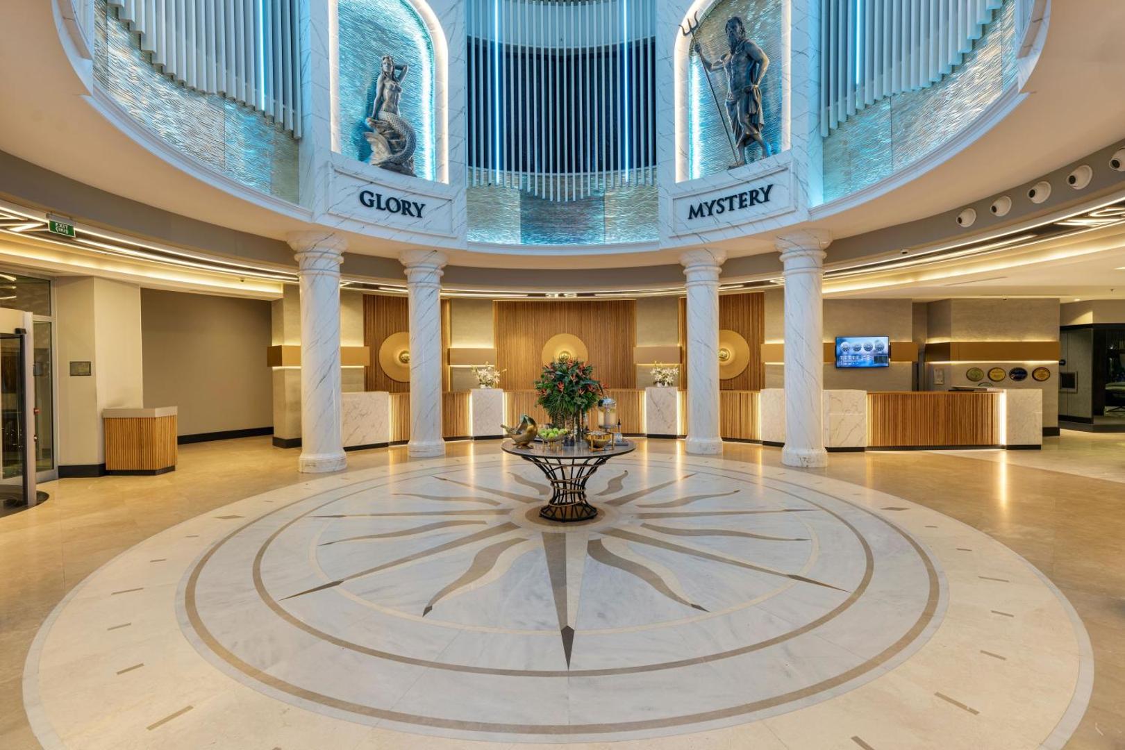 Viesnīcas Limak Atlantis De Luxe recepcija ar marmora saules simbolu uz grīdas un dekoratīvām kolonnām Belekas kūrortā.