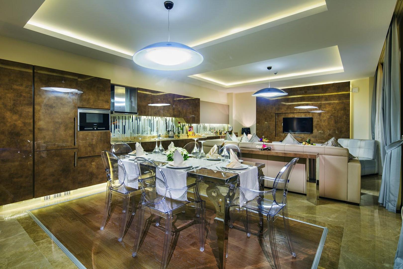 Bellis Deluxe Hotel eleganta ēdamistabas zona ar stikla galdu, caurspīdīgiem krēsliem un modernu virtuves iekārtu Belekā.