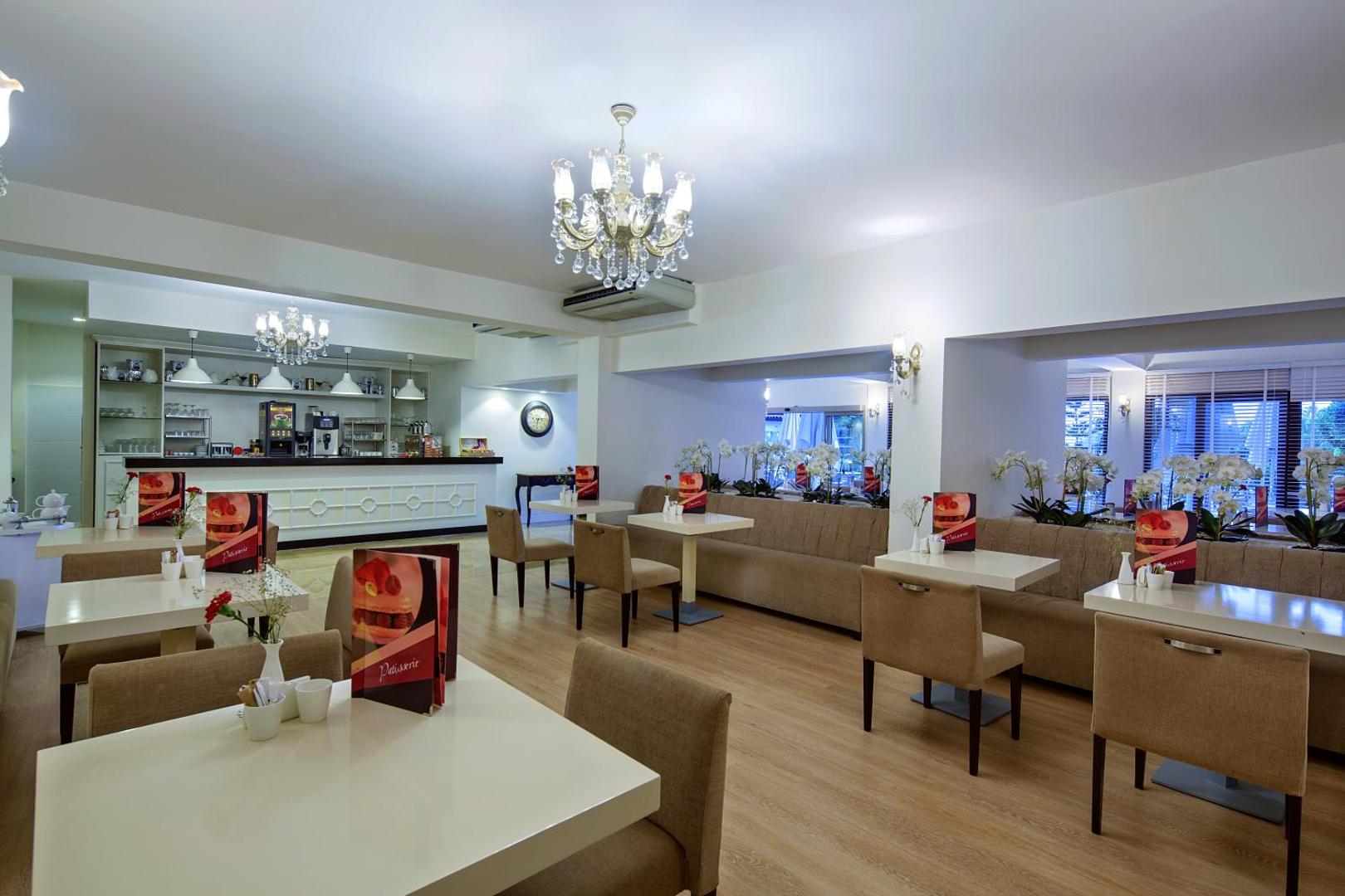 Bellis Deluxe Hotel kafejnīcas interjers ar elegantiem galdiņiem, mīkstajiem dīvāniem un bāra leti fonā — mājīga atmosfēra