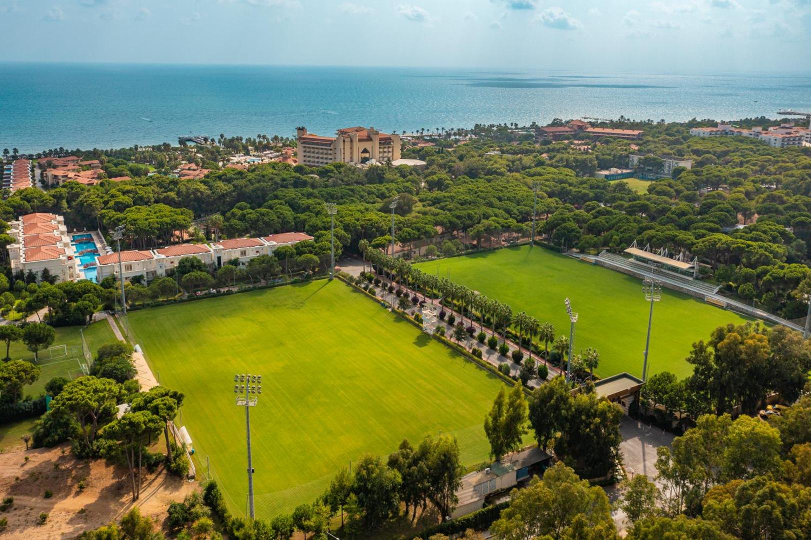 Bellis Deluxe Hotel aerofotoattēls ar futbola laukumiem, priežu mežu un Vidusjūras piekrasti Belekā, Turcijā — plaša zaļā teritorija