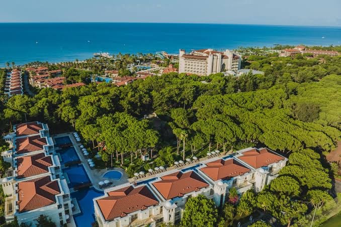 Bellis Deluxe Hotel teritorijas skats no augšas — villas ieskautas zaļojošos dārzos un priežu mežā pie zilas jūras krasta