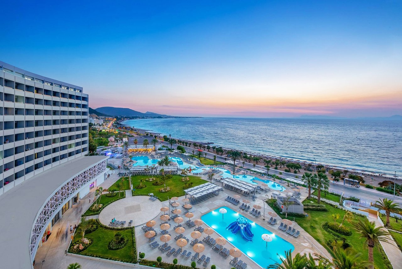Akti Imperial Deluxe Resort & Spa skats no augšas uz baseinu kompleksu un jūru saulrietā Rodas salā, Grieķijā