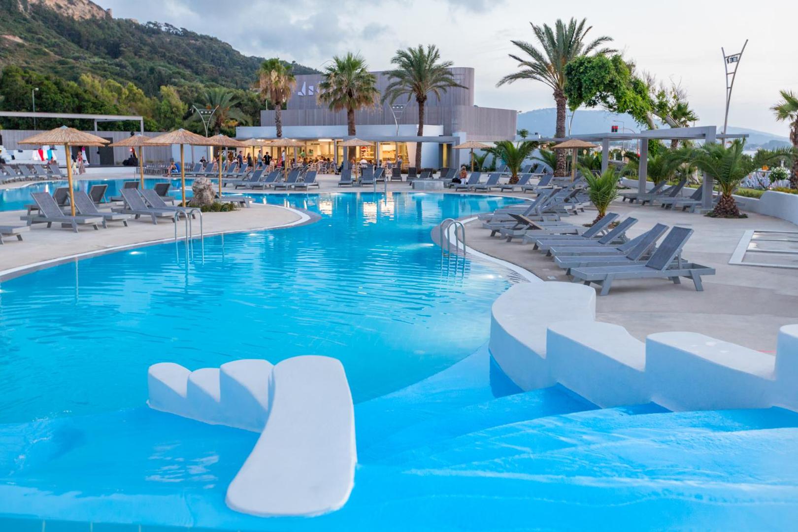 Akti Imperial Deluxe Resort & Spa galvenais āra baseins Rodas salā ar sauļošanās krēsliem, saulessargiem un palmu ieskautu atpūtas zonu