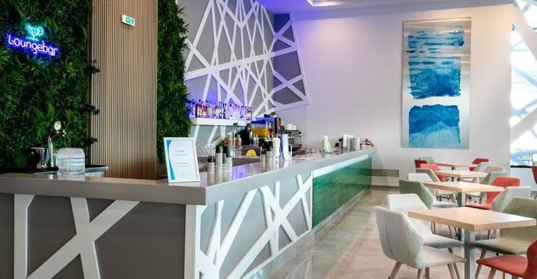 Akti Imperial Deluxe Resort & Spa modernais Loungebar ar gaišu interjeru, bāra leti, krāsainiem krēsliem un dekoratīvu zaļo sienu
