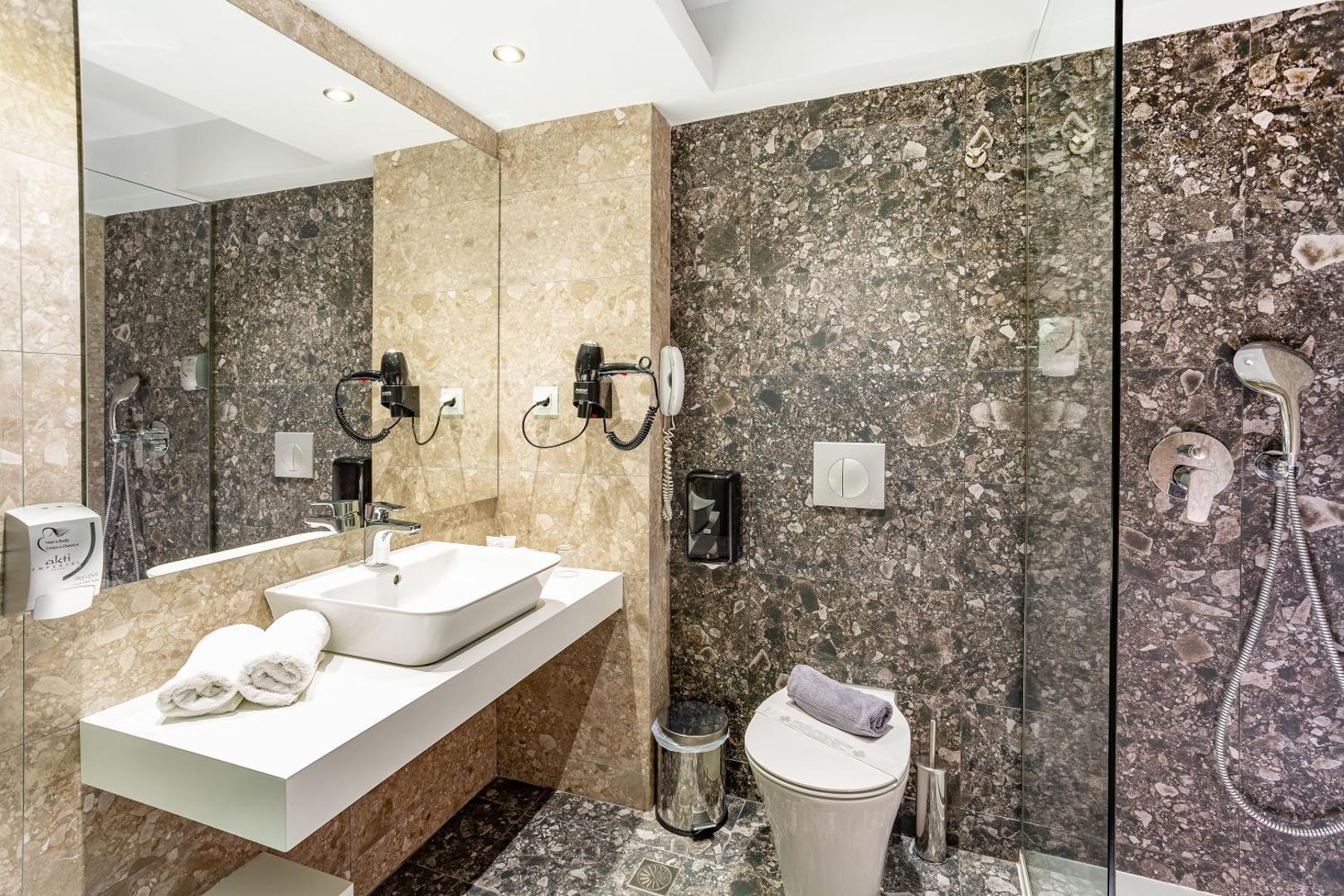 Viesnīcas Akti Imperial Deluxe Resort vannas istaba ar tumša akmens apdari, dušas zonu un fēnu pie sienas
