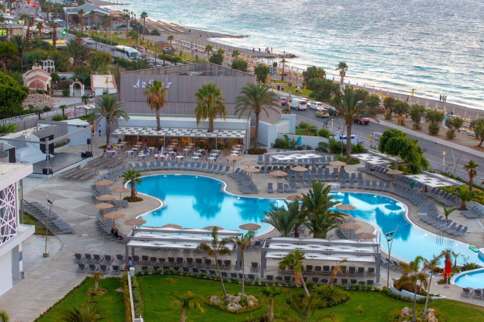 Skats uz Akti Imperial Deluxe Resort & Spa baseina zonu un āra restorāna terasi Rodas piekrastē saulrieta laikā