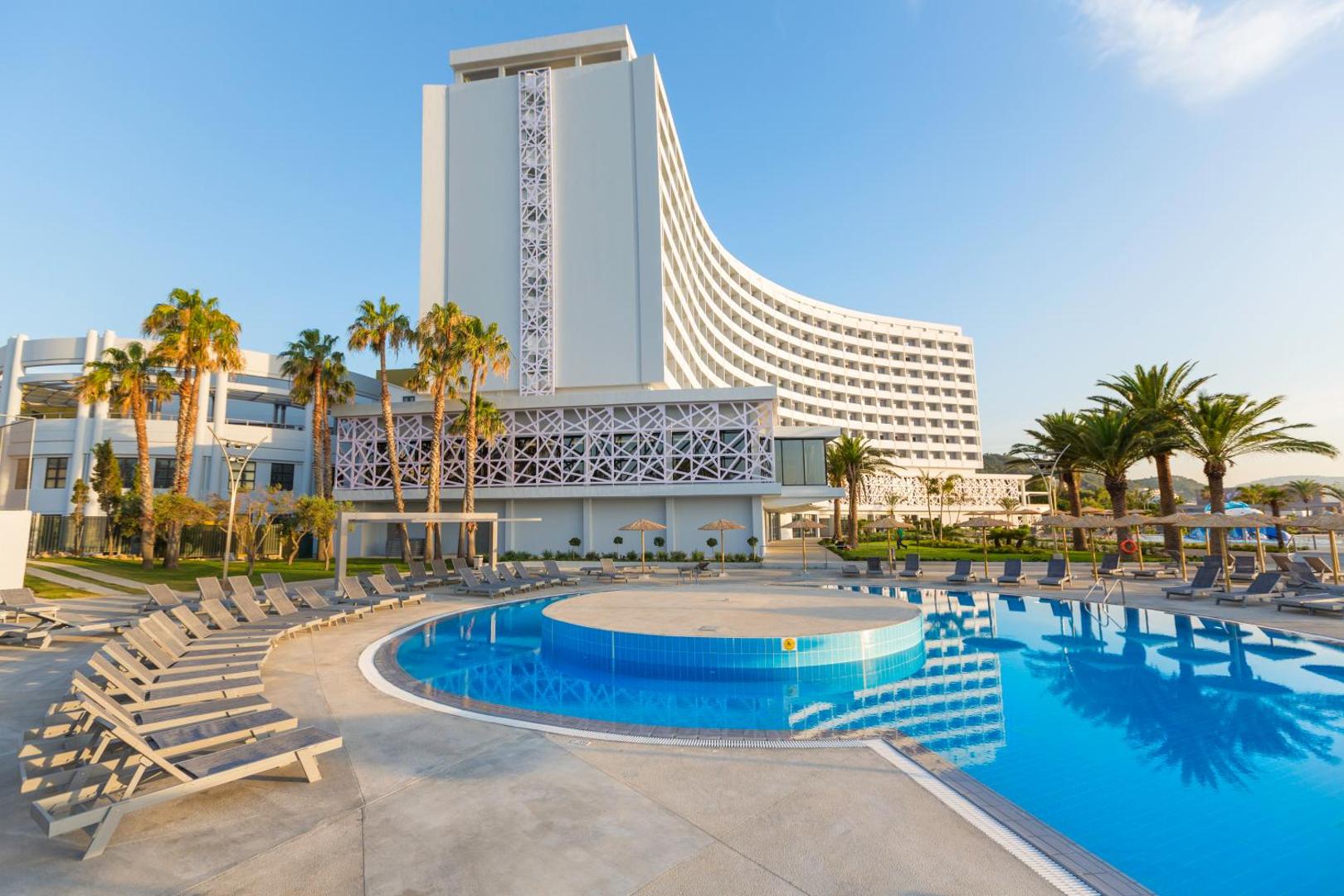 Akti Imperial Deluxe Resort & Spa modernā ēkas fasāde ar baseinu priekšplānā un sauļošanās krēsliem Rodas salā