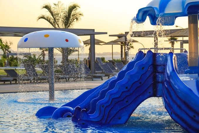 Akti Imperial Deluxe Resort & Spa bērnu baseins ar zilu slidkalniņu un sēnes formas strūklaku Rodas salā, Grieķijā saulrietā