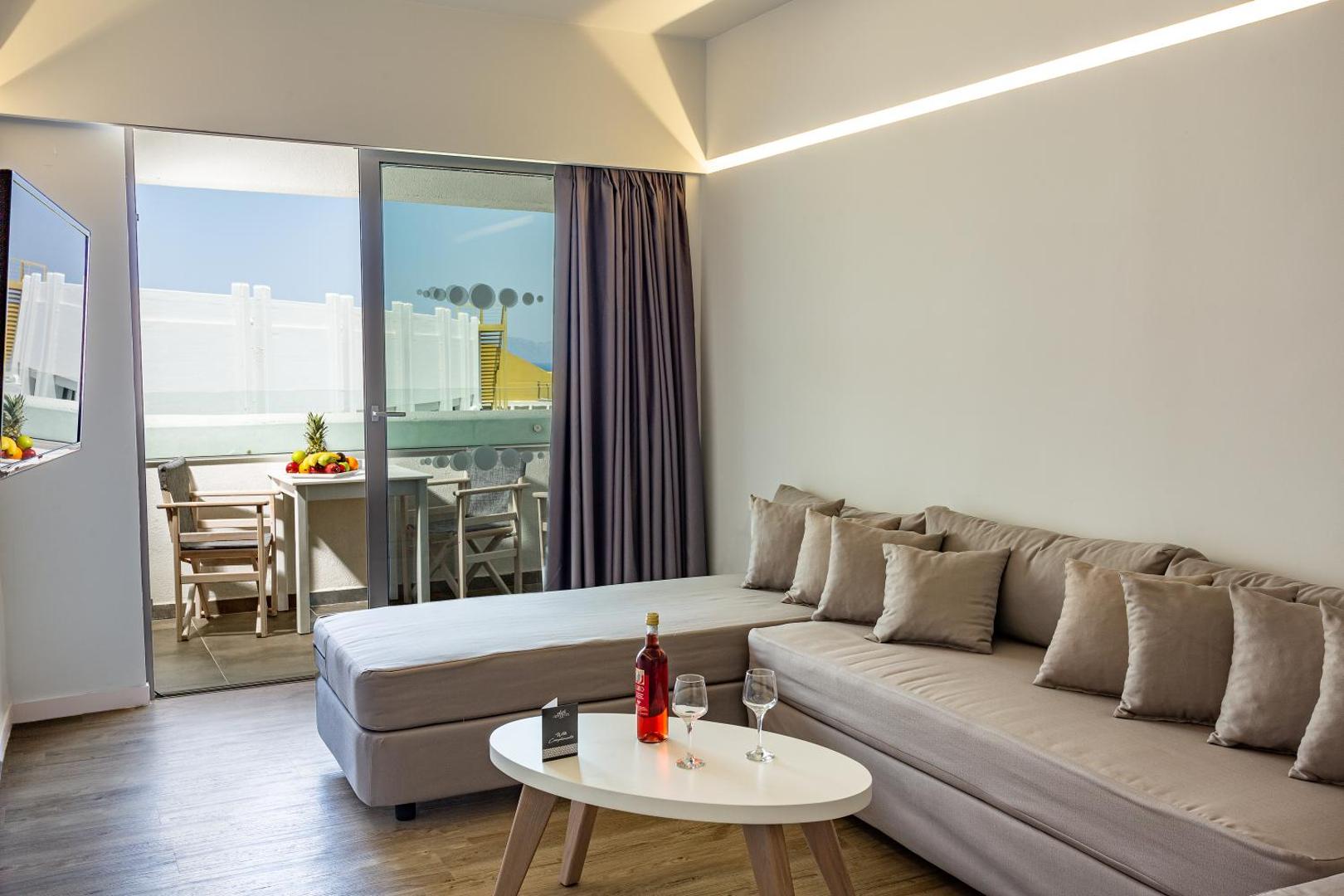 Akti Imperial Deluxe Resort viesnīcas numura viesistabas zona ar dīvānu, galdiņu un izeju uz balkonu Rodas salā