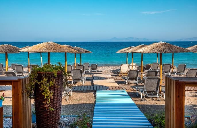 Akti Imperial Deluxe Resort privātā pludmale ar saulessargiem un zviļņiem Rodas piekrastē — skats uz tirkīzzilo jūru