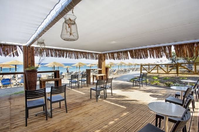Akti Imperial Deluxe Resort & Spa āra terase ar koka grīdu, modernām mēbelēm un skatu uz pludmales saulessargiem Rodas piekrastē