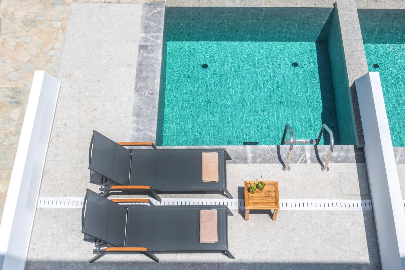 Aelius Hotel and Spa baseina zona no augšas ar diviem moderniem sauļošanās krēsliem un dzērieniem uz koka galdiņa
