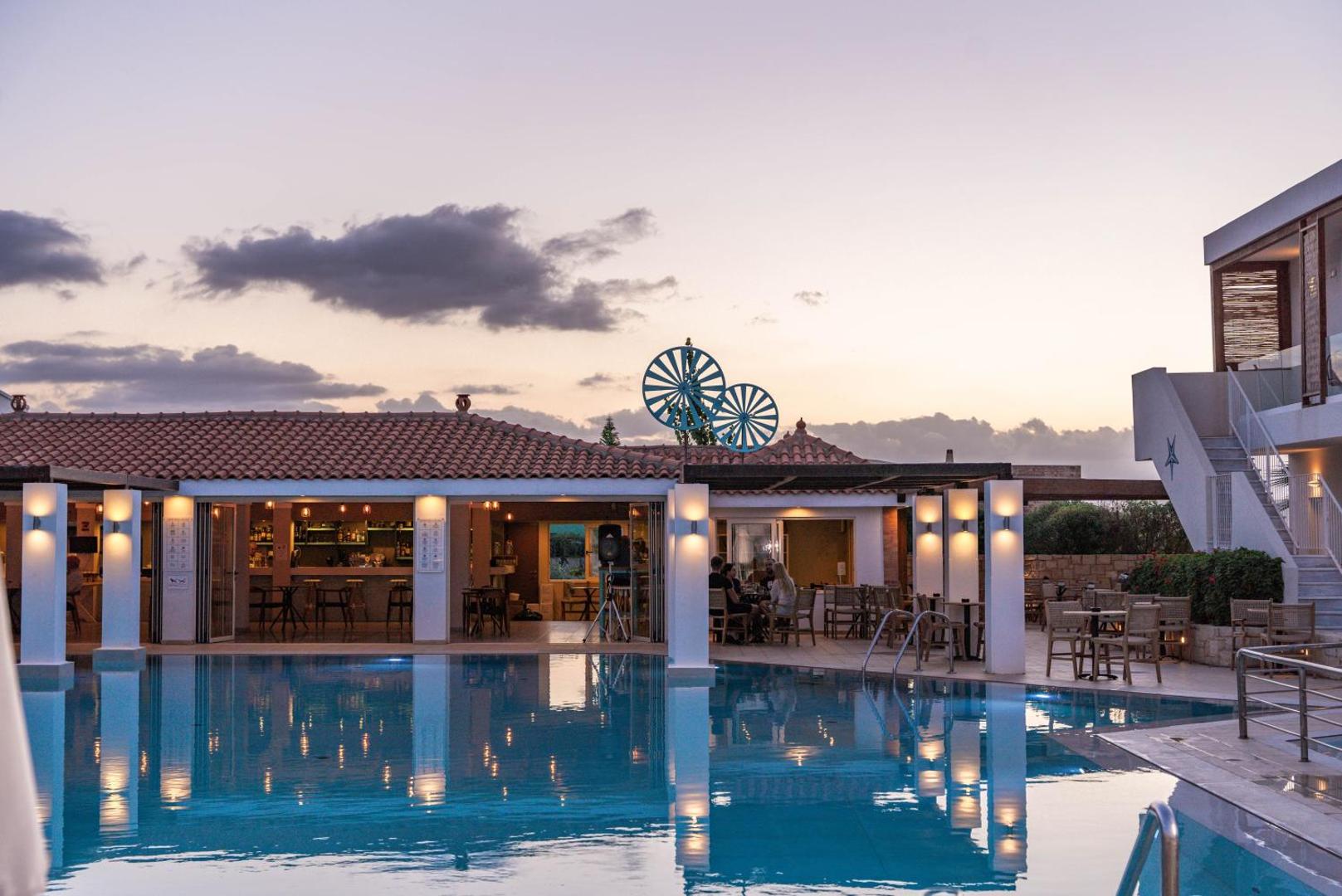Aelius Hotel and Spa baseina bārs un terase vakara apgaismojumā Krētā — baseina atspulgi un mājīga atmosfēra saulrietā.