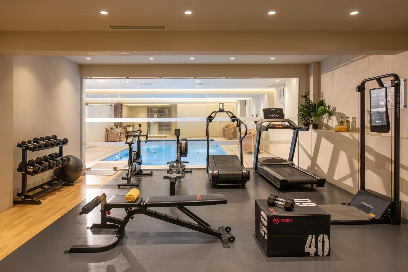 Aelius Hotel and Spa fitnesa centrs ar skrejceļiem, velotrenažieriem un brīvajiem svariem, fonā redzams iekštelpu baseins