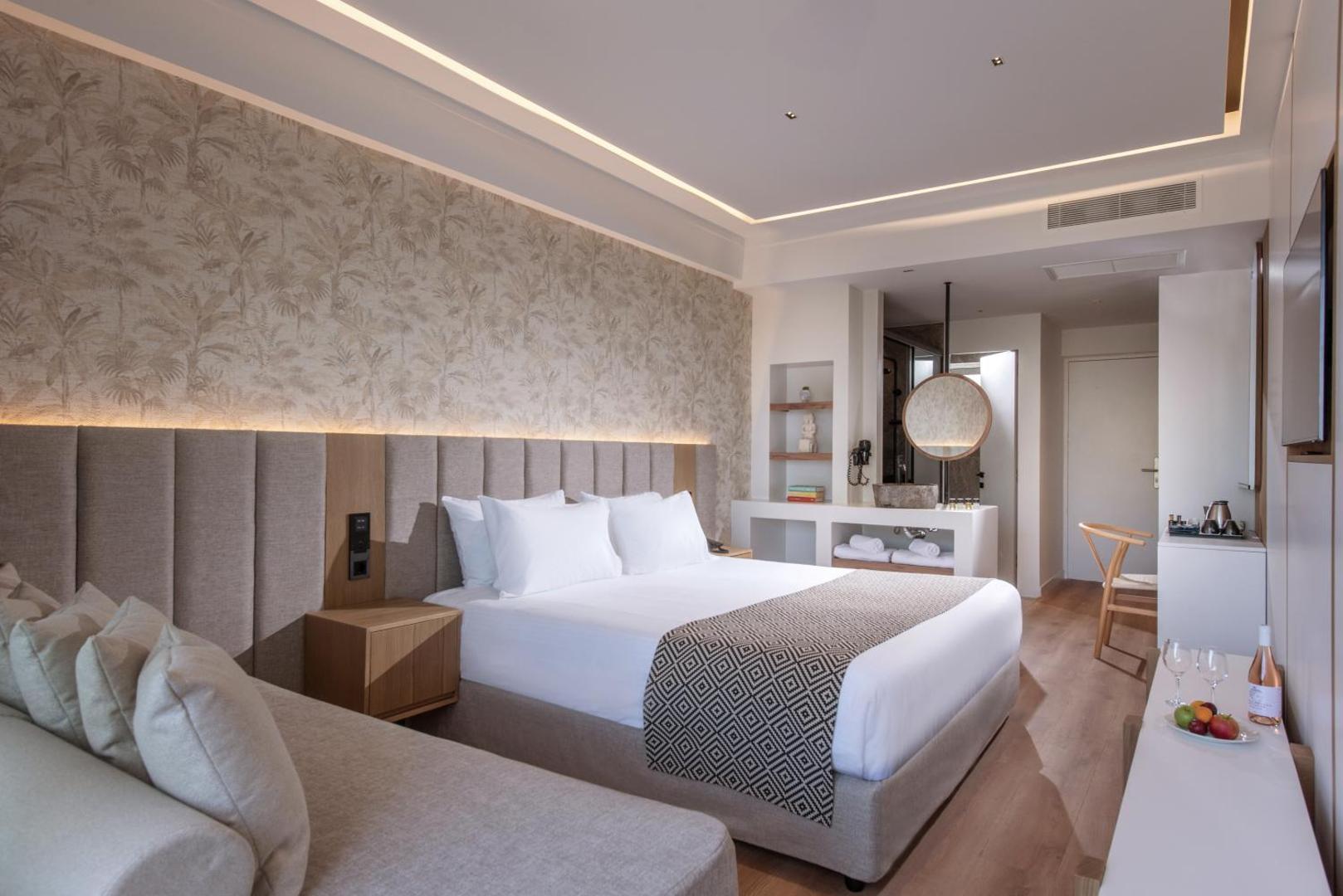 Aelius Hotel and Spa moderns divvietīgs numurs ar gaišu interjeru, koka elementiem un atvērtā plānojuma vannasistabas zonu Grieķijā