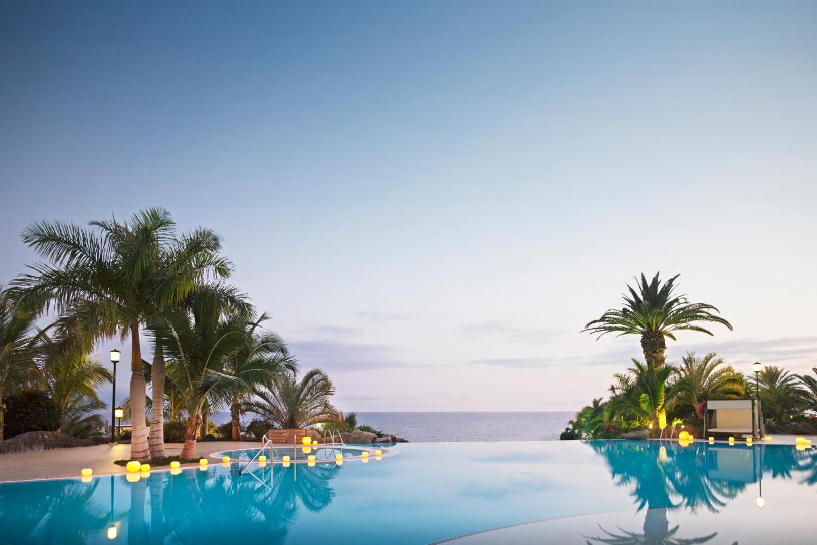 Roca Nivaria Gran Hotel bezgalības baseins krēslas stundā Tenerifē ar dekoratīvām gaismām, palmām un skatu uz Atlantijas okeānu