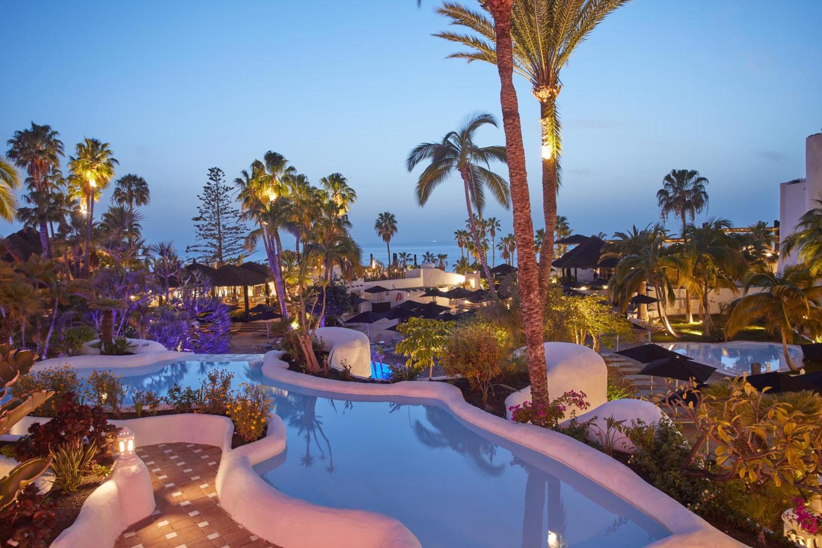 Dreams Jardin Tropical Resort & Spa vakara skats uz izgaismotiem baseiniem, palmām un viesnīcas dārzu Tenerifes piekrastē