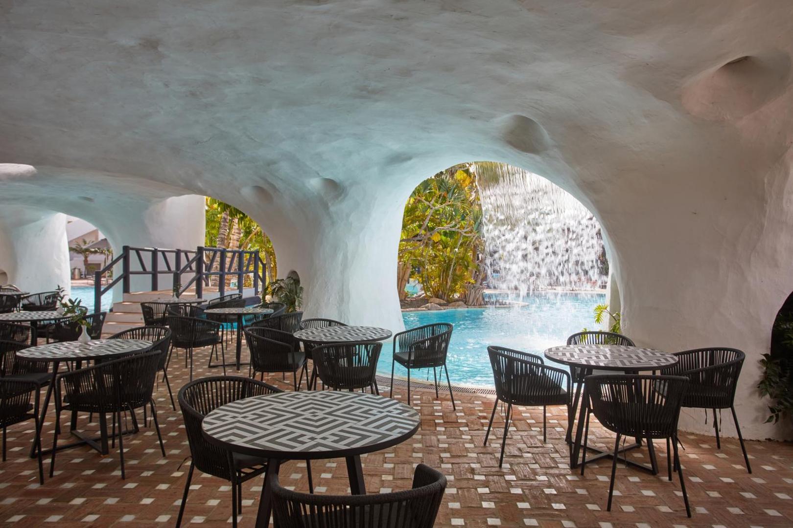 Viesnīcas Dreams Jardin Tropical Resort & Spa restorāna zona zem stilizētas alas velves ar skatu uz baseinu un ūdenskritumu