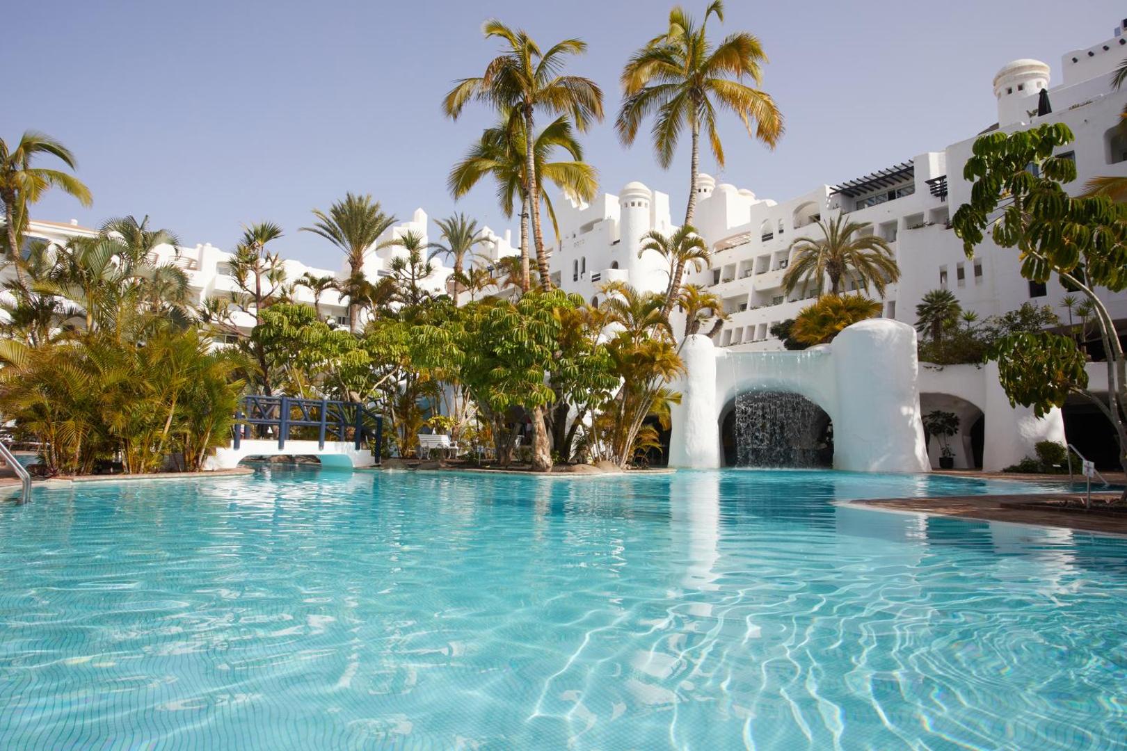 Dreams Jardin Tropical Resort & Spa galvenais baseins ar tiltiņu un baltu arhitektūru Tenerifē, Spānijā
