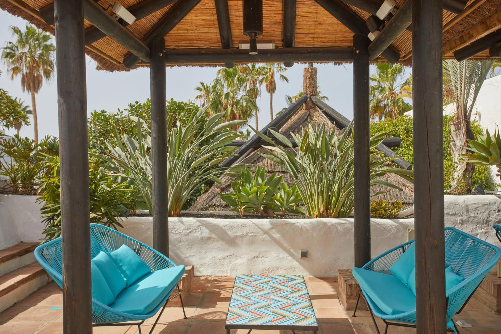 Dreams Jardin Tropical Resort & Spa atpūtas zona zem bungalo stila nojumes Tenerifē — zili pītie krēsli un tropu augi
