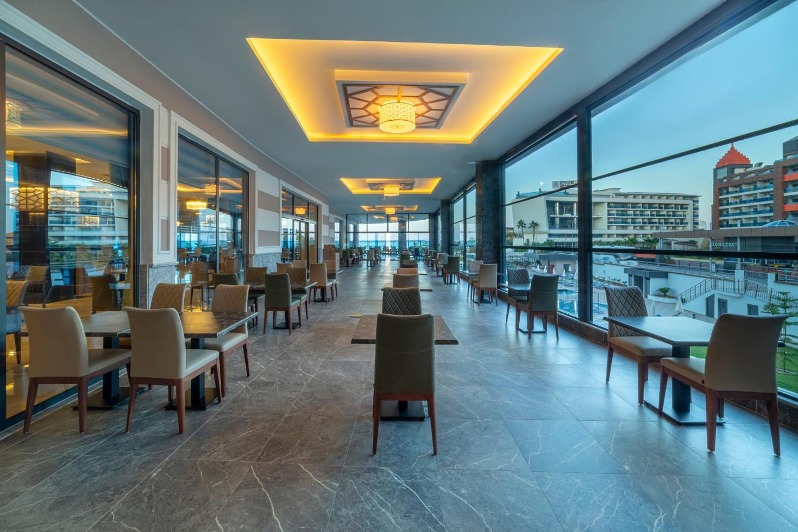 Lonicera Premium restorāna terase ar panorāmas logiem, skatu uz kūrorta teritoriju un modernām mēbelēm vakarā