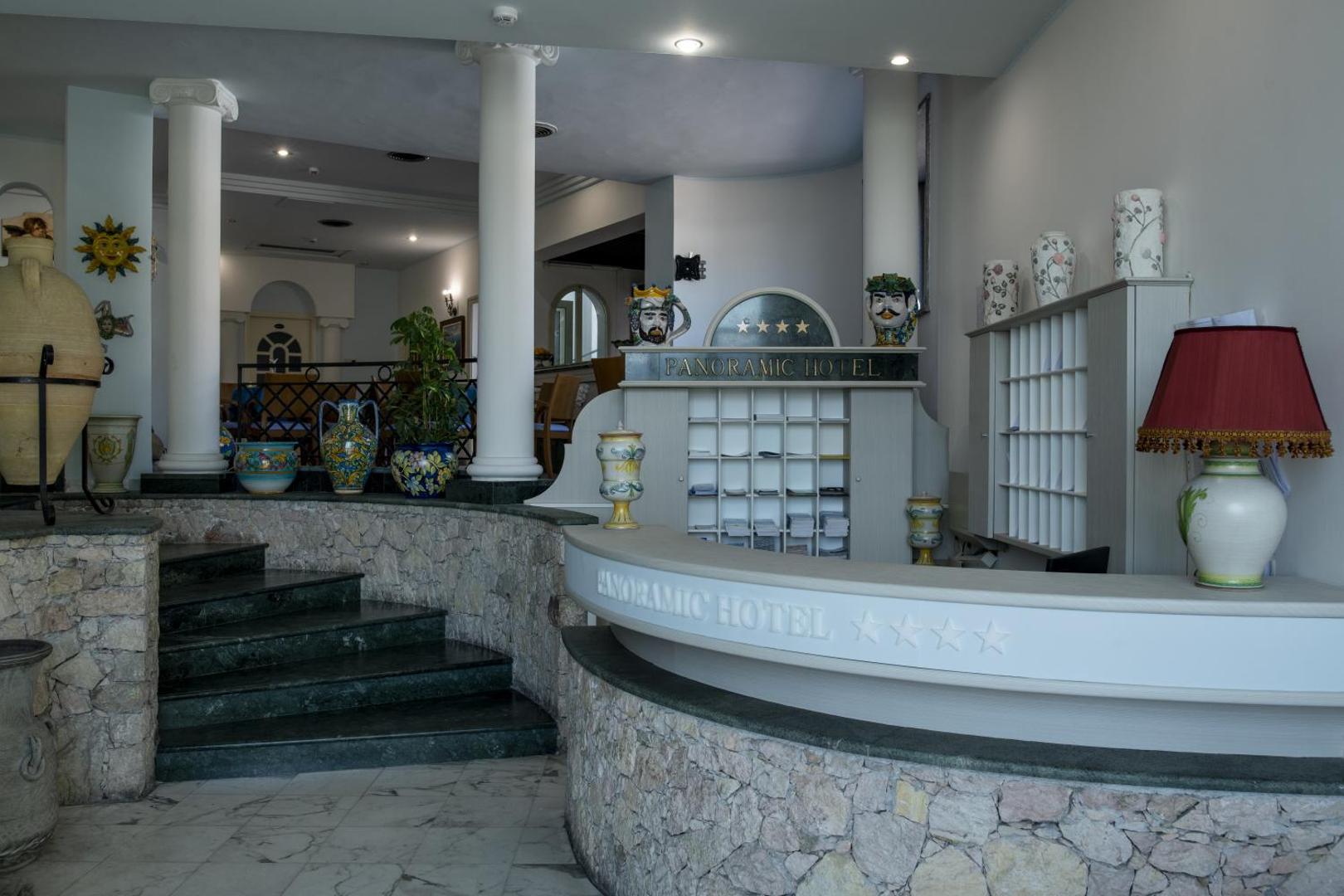 Viesnīcas Panoramic 4* recepcijas zona ar gaišu akmens apdari, dekoratīvām vāzēm un tradicionāliem Sicīlijas keramikas elementiem.