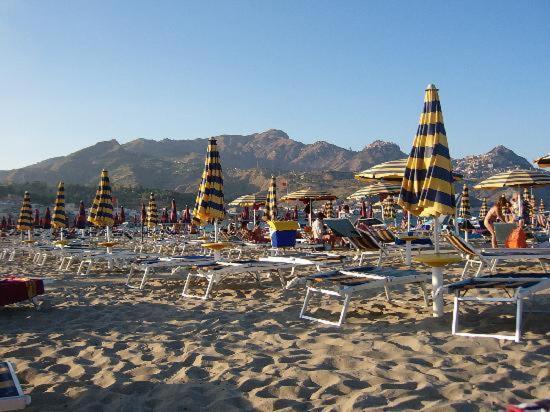 Giardini Naxos smilšu pludmale ar svītrainiem saulessargiem un skatu uz kalniem netālu no viesnīcas Panoramic Sicīlijā.