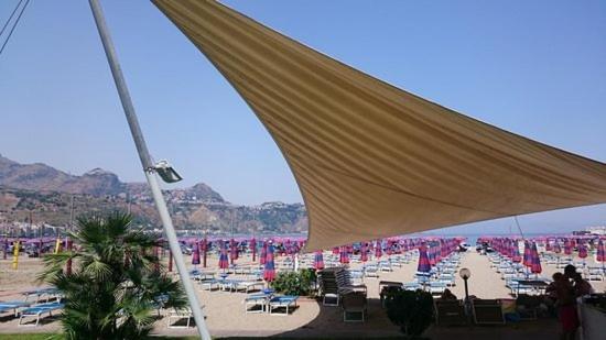 Skats uz plašu smilšu pludmali ar saulessargiem un atpūtas krēsliem netālu no viesnīcas Panoramic Giardini Naxos piekrastē.